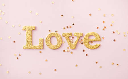 Golden shiny word Love and star shaped glitters on pastel pink background. Valentines day concept background.の写真素材
