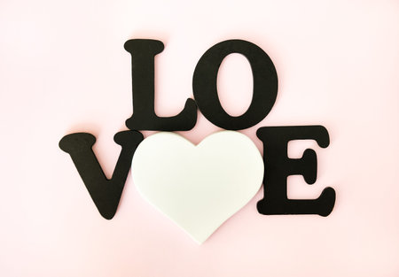 Black word Love and white heart on light pink background. Valentines day concept background.