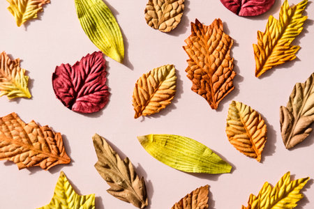Colorful red, yellow, orange paper leaves pattern on pastel pink background.
