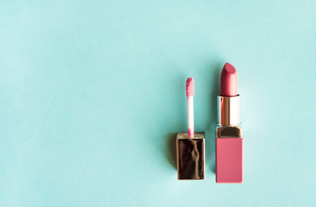Pink Lipstick and lip gloss brush on pastel blue green background. Make up products concept. 