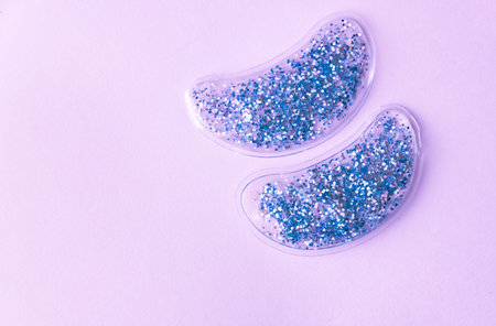 Silver glitter reusable cooling under eye pads on lilac background. Cosmetic products concept. 