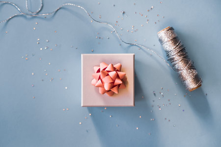 White silver gift box with pink bow on blue background in trendy flat lay composition with golden...