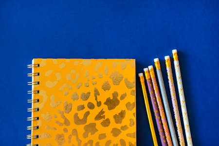 Pink notebook and cute golden pencils on trendy dark blue background. Flat lay minimalism style.の写真素材