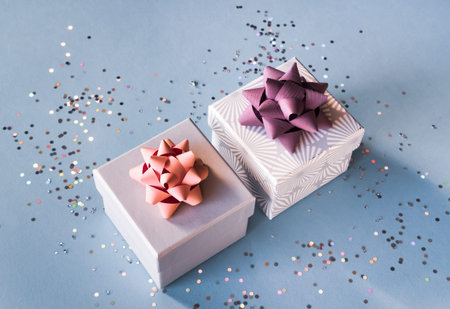 White silver gift boxes with pink bow on blue background in trendy flat lay composition with shiny...