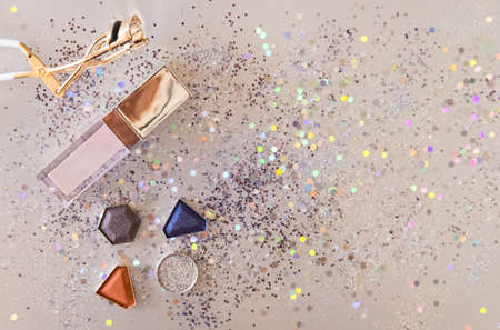 Assorted cosmetic products, eye shadows, lip gloss, eyelash curler on shiny beige background. Beauty concept. Flat lay design.の写真素材