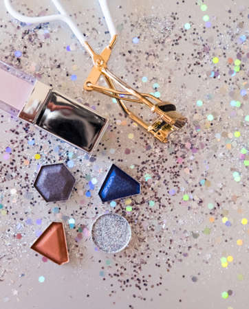 Assorted cosmetic products, eye shadows, lip gloss, eyelash curler on shiny beige background. Beauty concept. Flat lay design.の写真素材