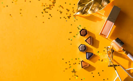 Assorted cosmetic products, eye shadows, lip gloss, eyelash curler on orange background. Beauty concept. Flat lay design.の写真素材