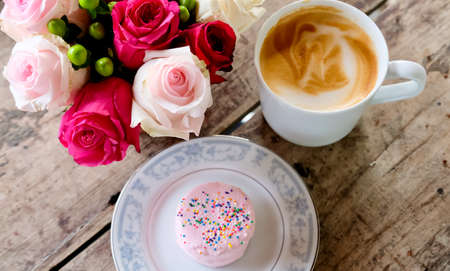 White cup of coffee latte, vanilla cake and pink roses on wooden table. Lifestyle concept. の写真素材