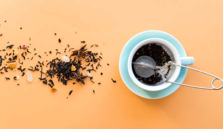 Tea preparing ceremony, mint green cup, tea-strainer and black fruit herbal dry tea on orange background. の写真素材