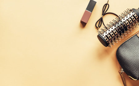 Brown cosmetic bag and hairbrush and lipstick on pastel yellow background. Beauty concept. Flat lay...