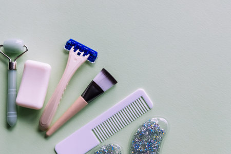 Skin care products: jade roller, brush, eye pads, razor on gray background. Beauty and makeup...
