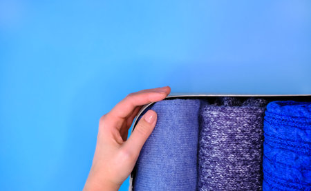 Blue knitted sweaters in textile basket and womans hand. Order in wardrobe, clothes concept.