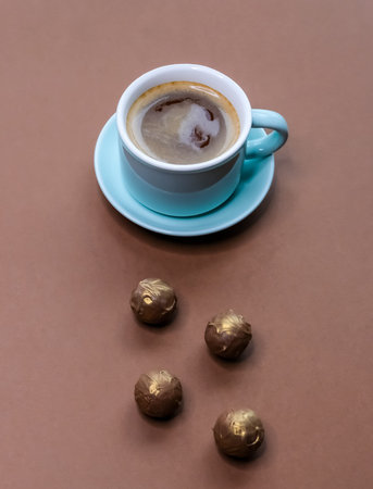 Coffee espresso in mint green cup with dark chocolate truffles on brown background. 