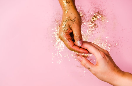 Women's hands and golden glitters on pink background. Festive flat lay concept.