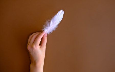 Pink feather in woman's hand on brown background. Flat lay style. 
