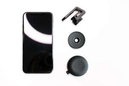 Black cellphone and macro lens, metal screw clip and silicon case on white background. Modern hobby...