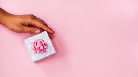 Women's hand and gift box on pink background. Festive flat lay concept.