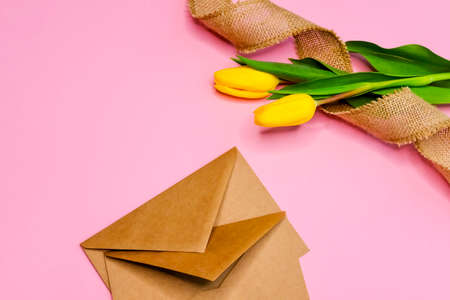 Two kraft paper envelopes, yellow tulips and burlap ribbon on pink background. Romantic festive concept.の写真素材