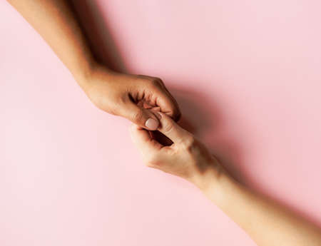 Black and white women holding hands on pastel pink background. Minimal flat lay concept.の写真素材