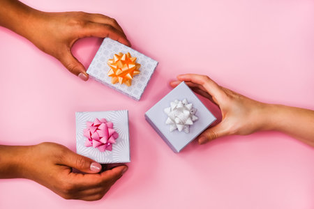Women's hands and gift boxes on pink background. Festive flat lay concept.