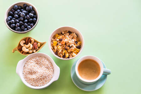 Cup of coffee espresso, nuts mix, blueberries, amaranth and muesli on mint green background. Heathy breakfast concept.の写真素材