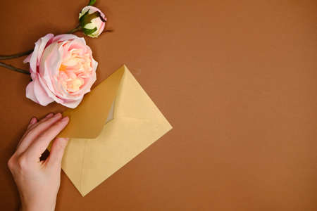 Golden envelope, artificial pink rose and woman's hand on brown background with golden confetti glitters. Flat lay style.の写真素材