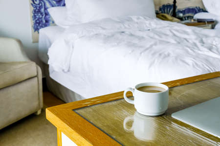 White cup of coffee and silver laptop on wooden table in hotel room. Working and traveling concept.の写真素材