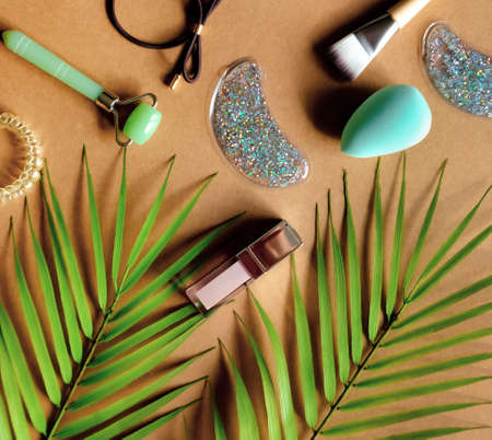 Cosmetic products: lip gloss, lipstick, jade roller, brush, patches on natural brown background. Beauty and makeup concept. Flat lay design.の写真素材