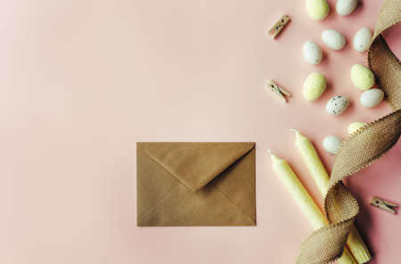 Creative Easter layout. White and yellow mini eggs, kraft paper envelope and candles on beige pastel background. Spring holidays concept.の写真素材