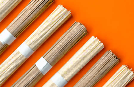 Uncooked ramen and soba noodles on vivid orange background. の写真素材