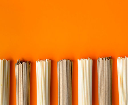 Uncooked ramen and soba noodles on vivid orange background. 