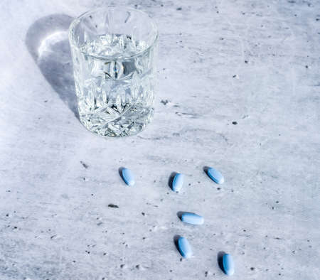 Medicine pills and capsules with glass of water on gray background.の写真素材
