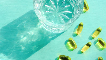 Medicine pills and capsules with glass of water on turquoise background.