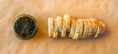 Natural sturgeon Black Caviar in glass bowl and fresh baguette on pastel background banner.