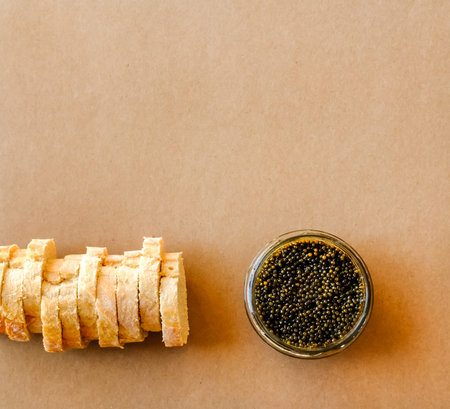 Natural sturgeon Black Caviar in glass bowl and fresh baguette on pastel background.