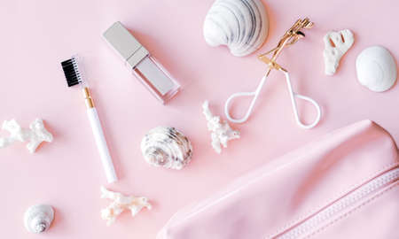 Cosmetic products: pink and white lip gloss, bag, brush and eyelash curler on pastel background. Beauty and makeup concept. Flat lay design.の写真素材