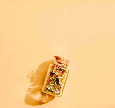 Golden paper clips in glass jar on pastel orange background. Back to school concept. の写真素材
