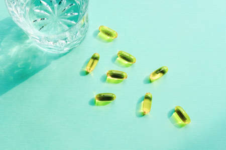 Medicine pills and capsules with glass of water on turquoise background.の写真素材