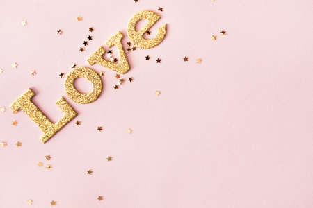 Golden shiny word Love and star shaped glitters on pastel pink background. Valentines day concept background. の写真素材