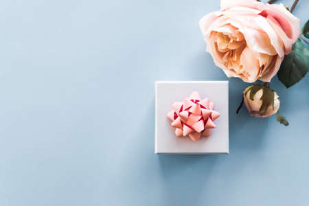 Artificial roses and gift box with pink bow on pastel blue background. Mockup. Office concept. の写真素材