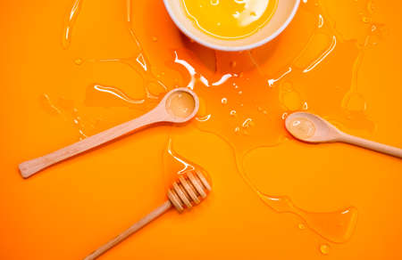 Agave syrup in bowl and wooden honey dipper, spoons on vivid orange background.の写真素材