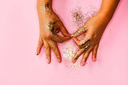 Woman&#39;s hands and golden glitters on pink background. Festive flat lay concept.の写真素材