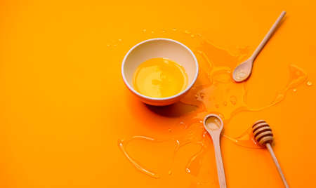 Agave syrup in bowl and wooden honey dipper, spoons on vivid orange background.の写真素材
