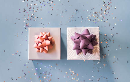 White silver gift boxes with pink and purple bows on blue background in trendy flat lay composition with shiny glitters.の写真素材