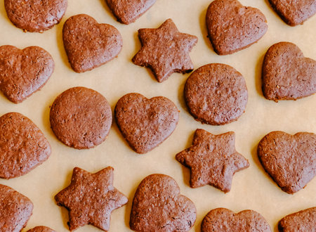 Freshly baked chocolate cookies heart and star shaped on brow baking paper on wooden table.