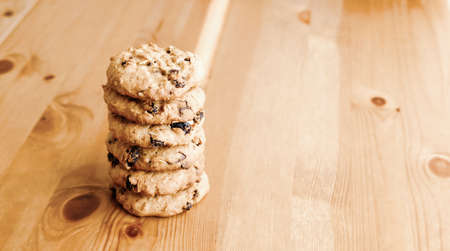 Freshly baked oatmeal cookies with raisins, almonds and chocolate on wooden table.の写真素材