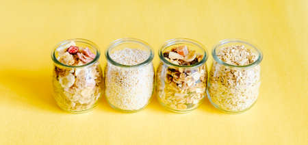 Breakfast cereal ingredients in glass jars on yellow background. Ready-to-eat fast food concept.の写真素材