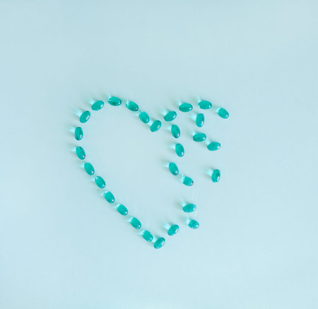 Mint blue liquid gel capsules in heart shape on pastel green background.