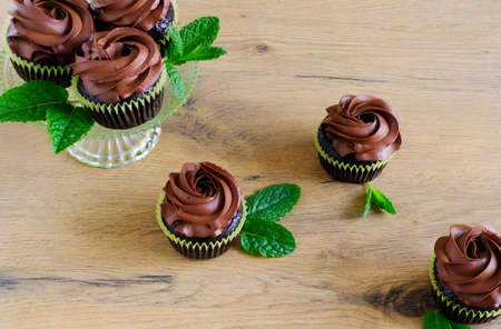Dark chocolate coffee cupcakes and mint leaves on wooden brown table background. Sweet food concept. の写真素材