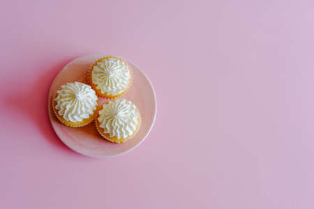 Vanilla cupcakes with cream cheese frosting and a cup of coffee on pink background. Sweet food concept. の写真素材